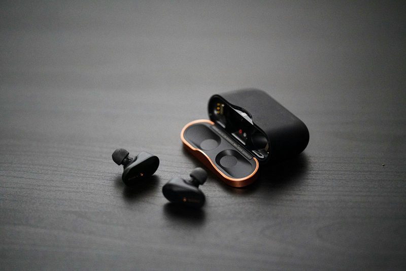 Black wireless earbuds and a copper-rimmed case on a dark desk